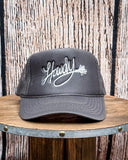 Front view of the Embroidered Rope Howdy Trucker Cap displayed on a wood table, wood backdrop.