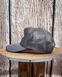 Side view of the Embroidered Rope Howdy Trucker Cap displayed on a wood table, wood backdrop.