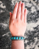 The Rayna Genuine Turquoise Bracelet displayed on a hand with cowhide in the background.