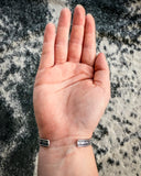 Back view of the Abha Genuine Turquoise Bracelet displayed on a hand with cowhide in the background.