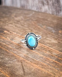 The Riley Adjustable Genuine Turquoise Ring sitting on a wood table.