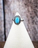 The Riley Adjustable Genuine Turquoise Ring on a display stand with a wood backdrop.