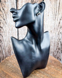 The Naja Genuine Turquoise Earrings on a mannequin, sitting on a wood table with a wood backdrop.