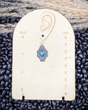 The Leif Genuine Turquoise Earrings displayed on a ruler showing size, sitting on beans and wheat.