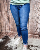 A girl modeling the Midnight Range Skinny Jeans while standing on cowhide, wood backdrop.