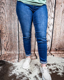 A girl modeling the Midnight Range Skinny Jeans while standing on cowhide, wood backdrop.