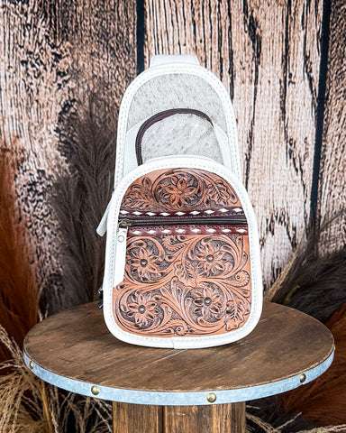 Front view of the Ridge Bloom Tooled Sling Bag - Ivory on a wood backdrop.