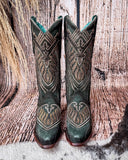Front view of the Mystic Pine Corral Boots with a wood backdrop.