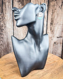 The Bitty Blue Stud Fashion Earrings displayed on mannequin in front of wood backdrop.