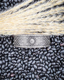The Sable Sun Cuff Fashion Bracelet displayed on black pebbles and wheat.