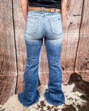 Person wearing blue jeans with a patterned belt against a wooden background