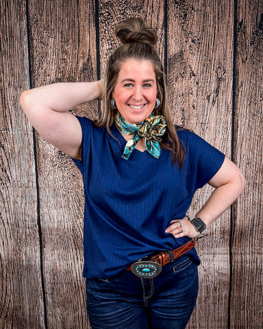 The Thatcher Top in navy being styled and modeled on a women in front of wood background.
