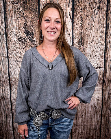 The Hadley Top in Charcoal being styled with jeans and worn by a women in front of wood background.