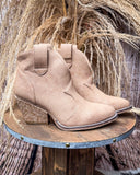 Dangerous Ankle Bootie in Light Tan displayed on wooden table in front of wheat background.