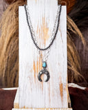 Jericho Layered Squash Blossom Fashion Necklace displayed on wood in front of wheat background.