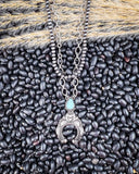 Jericho Layered Squash Blossom Necklace being displayed on black pebbles and wheat background.