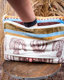 The Cactus Stripe Travel Blanket on a wooden table with a hand entering the opening in the middle. 