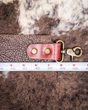 Brown leather purse strap and brass clasp on a fur background, measured with a ruler.