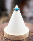 Ring with turquoise stone on a white cone-shaped stand on a wooden surface