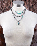 Necklace with faux turquoise beads and silver pendant on a mannequin against a wooden background