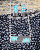 Necklace and earrings with faux turquoise floral designs on a bed of black beans.
