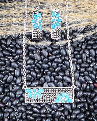 Necklace and earrings with faux turquoise floral designs on a bed of black beans.