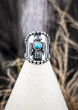 Silver ring with a faux turquoise stone on a white stand against a natural background