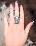 Hand wearing a silver ring with a faux turquoise stone against a blurred background