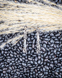 Silver earrings on a bed of black beans and dried grasses
