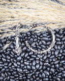 Silver hoops on a bed of black beans with wheat stalks in the background