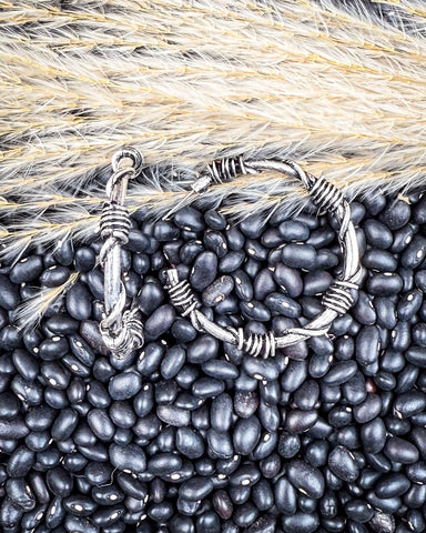 Silver hoops on a bed of black beans with wheat stalks in the background