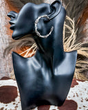 Barbed wire hoop earring on a black mannequin ear with a rustic background