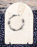 Silver hoop earring on a measurement card with black beans in the background
