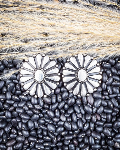 Silver floral earrings on a background of black beans and straw.