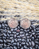 Pair of earrings with intricate designs on a bed of black beans and straw.