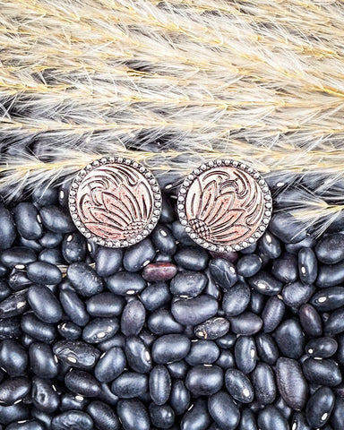 Pair of earrings with intricate designs on a bed of black beans and straw.