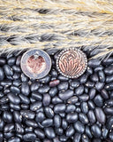 Two earrings with intricate designs on a bed of black beans and straw.