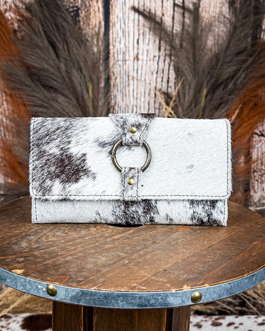White and black cowhide wallet with brass ring detail on a wooden surface