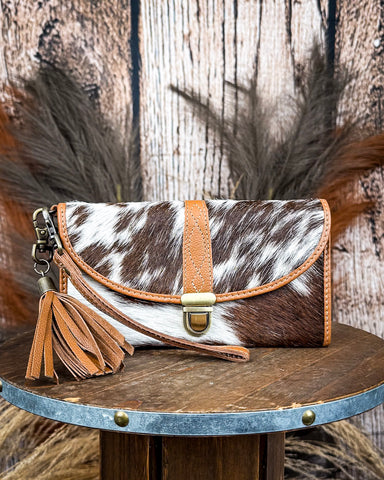 Cowhide leather clutch with brown accents on a wooden surface