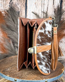 Brown leather wallet with cowhide pattern strap on a wooden surface