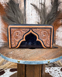 Tooled leather wallet on a wooden surface with a rustic background