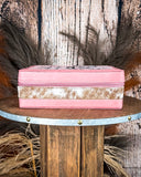 Pink jewelry box with cow hide accents on a wooden surface with decorative elements.
