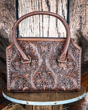 Brown leather handbag with intricate floral patterns on a wooden surface.