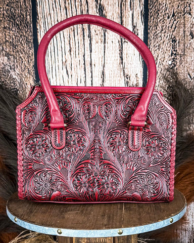 Red leather handbag with floral patterns on a wooden surface