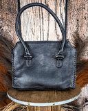 Black leather handbag on a wooden stool with a rustic background