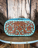 Turquoise and brown tooled leather make up bag on a wooden surface with a rustic background