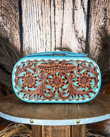 Turquoise and brown tooled leather make up bag on a wooden surface with a rustic background