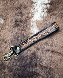 Decorative leather key fob with floral patterns on a textured brown surface