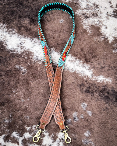 Turquoise and brown leather purse strap laying on cowhide