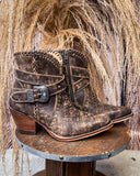 Brown leather boot with decorative buckle on a wooden stand against a rustic background